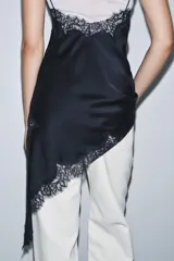 Vestido corto de satén con escote en pico y tirantes finos. Presenta aplicaciones de encaje en el escote y en el bajo, con un diseño asimétrico y abertura lateral.