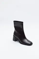 Bota corta de caña elástica, color negro con acabado charolado. Presenta puntera cuadrada y taco medio geométrico y ancho.