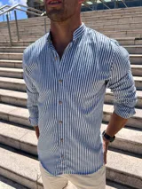 Camisa de hombre a rayas verticales azul marino y blanco, con cuello mao y manga larga. Cierre frontal con botones de madera.