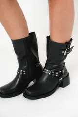 Bota biker de caña media color negro, con hebilla en la parte superior y detalle de aro y tachas en la parte inferior.