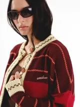 Cardigan tejido de punto jacquard en tonos bordó y rojo con rayas, de corte oversize, cuello redondo y cierre frontal con botones carey. Presenta detalles bordados en contraste y monograma en la espalda.