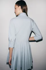 Vestido corto tipo camisero de algodón, con cuello solapa, mangas tres cuartos y cierre frontal con botones. Presenta bolsillos de plastrón con solapa en el pecho y falda con bajo plisado.