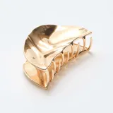 Set de dos pinzas para el pelo de metal dorado con diseño de concha marina, una con acabado liso y otra con estructura calada.