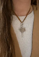 Collar con dije de cruz de diseño abstracto compuesto por múltiples varillas metálicas plateadas, suspendido de un cordón de gamuza color marrón.