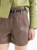 Short Amy confeccionado en cuero ovino color marrón, de tiro alto con silueta evasé, calce entallado en la cintura, recortes verticales y bolsillos traseros, complementado con un cinturón de cuero.