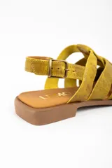 Sandalia tipo cangrejera de cuero lavado color mostaza, con diseño de tiras cruzadas, puntera cerrada y cierre con hebilla metálica en el tobillo. Cuenta con suela plana de goma.