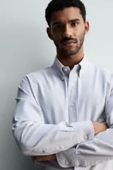 Camisa de corte regular fit confeccionada en tejido de algodón con efecto lavado. Presenta cuello abotonado, manga larga con puños abotonados, bolsillo en el pecho y cierre frontal con botones.