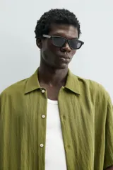 Camisa de corte relajado confeccionada en tejido fluido de lyocell y viscosa, color verde oliva. Presenta cuello solapa, manga corta, cierre frontal de botones y dos bolsillos plastrón en la parte inferior.
