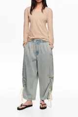 Pantalón jogger de denim celeste claro, confeccionado en mezcla de lyocell y algodón, con tiro bajo, cintura elástica y bajos fruncidos con tiras ajustables.