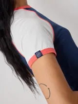 Remera estilo raglan de manga corta, con cuerpo azul marino, mangas blancas y ribetes en color salmón. Cuenta con un estampado frontal ovalado con diseño gráfico y texto.