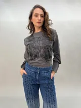 Remera negra de algodón con estampado dorado que simula un tejido o collar sobrepuesto. Presenta una moldería que realza los hombros y se entalla levemente hacia la cintura.