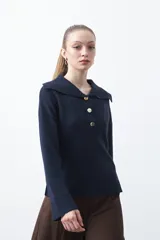 Sweater de tejido de punto color azul marino, con cuello polo amplio y cierre frontal con tres botones metálicos. Presenta mangas largas levemente acampanadas y un diseño de silueta relajada con aberturas laterales en el ruedo.