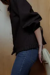 Blusa negra con cuello bebé con volados, mangas 3/4 abullonadas con lazo y botones blancos.