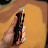 Billetera tarjetero de cuero sintético color negro con costuras en contraste color naranja. Cuenta con cierre lateral mediante broche a presión y diseño compacto.