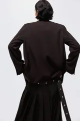 Blazer color marrón oscuro con cuello elevado, hombreras, abertura en los puños y bolsillos delanteros ribeteados. Incluye un cinturón fino con hebilla metálica para ajustar la cintura.