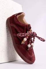 Zapatillas urbanas de gamuza color marrón, con diseño de cordones decorados con cuentas de piedra y detalles de líneas brillantes en los laterales. Presentan suela de goma texturizada al tono.