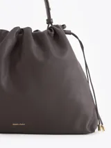 Cartera tipo shopper de cuero vacuno color tostado, con formato amplio, fruncido superior y cordones ajustables a los lados. Cuenta con tiras finas para llevar al hombro y sutil grabado de la marca en el frente.