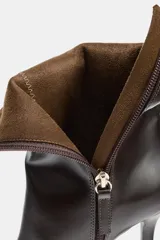 Botín de cuero color marrón oscuro, con tacón fino alto, punta fina y cierre lateral. Presenta un diseño minimalista con costuras visibles en el empeine.