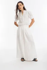 Pantalón blanco de lino, corte palazzo, tiro medio-alto, con tablas delanteras, elástico en la parte trasera y bolsillos laterales.