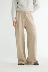 Pantalón de tejido de punto color beige, de corte recto y holgado, con cintura elástica y cordón de ajuste. Presenta costuras verticales frontales que recorren el largo de las piernas.