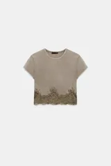 Top crop de cuello redondo y manga corta, confeccionado en tejido de algodón con efecto lavado. Presenta un bajo decorado con encaje a tono.