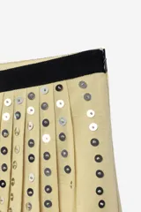 Falda de tiro medio confeccionada en hilatura de lino, color beige con bloques negros y detalles de abalorios y ojales metálicos aplicados a contraste. Cuenta con cierre lateral con cremallera oculta en costura.