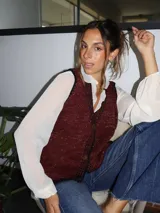 Chaleco tejido color tostado con destellos de lurex, escote en V y cierre frontal con botones. Presenta detalles de bordados y terminaciones en crochet en color crudo.