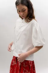 Camisa de popelina de algodón con cuello mao, botones frontales agrupados en pares y mangas cortas abullonadas tipo balloon. Cuenta con un diseño estampado de patrón geométrico y floral sobre fondo negro.