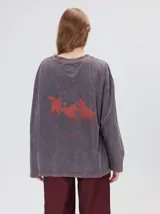 Remera oversize de manga larga color naranja con efecto gastado, cuello redondo y gráfico estampado en la espalda.