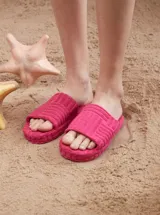Sandalias planas tipo chinela color fucsia, confeccionadas en tejido estilo toalla con diseño texturizado de franjas y suela plana.