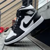 Championes Nike Air Jordan 1 Mid, diseño de caña media con combinación de colores blanco y negro. Presentan el icónico logo Swoosh en los laterales, el logotipo Air Jordan Wings en el cuello y una suela de goma resistente.