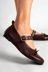 Chatas de cuero color chocolate, con punta redondeada, tira sobre el empeine con hebilla plateada y pequeño moño decorativo en la punta.