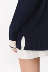 Sweater de punto color marrón con cuello polo en contraste color crema. Presenta diseño de rayas verticales texturizadas, mangas largas con puños en color crema y corte holgado.