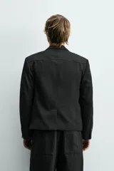 Blazer de corte cropped confeccionado en tejido con viscosa, color negro. Presenta cuello con solapas de muesca, cierre frontal de tres botones, mangas largas con puños abotonados y bolsillos de vivo en la cadera.