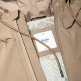 Campera con capucha color beige, con cierre frontal, bolsillos laterales y logo bordado en el pecho. Cuenta con membrana TPU impermeable y costuras selladas.