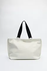 Bolso negro tipo shopper de símil cuero con terminación suave. Tiene asas anchas de cinta y un bolsillo frontal con solapa.