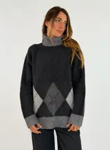 Sweater de cuello alto con diseño de rombos en la parte inferior. Presenta una combinación de tonos grises y negros con detalles de líneas finas en color rojo. Posee puños y ruedo acanalados en color gris claro.