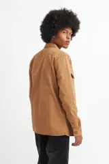 Camisa marrón de manga larga con cuello clásico, cierre frontal con botones, dos bolsillos con solapa abotonada en el pecho y puños abotonados.