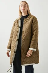 Campera larga color marrón con interior de sherpa color crema, reversible y capitoneada con patrón de rombos.