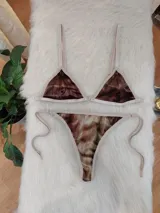 Bikini de dos piezas con corpiño triangular y bombacha de atar, confeccionado en tela de terciopelo elástico con estampado degradé en tonos marrones. El corpiño tiene un broche trasero y breteles regulables, y la bombacha es de corte less brasilero con tiras laterales ajustables.