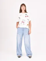 Remera de manga corta color beige claro, con cuello redondo y estampado floral en tonos dorados y plateados. Las mangas tienen un detalle de tejido acanalado.