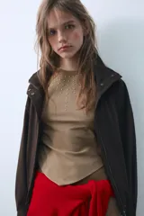 Top sin mangas de algodón color tostado, con cuello redondo y detalle de tachas metálicas en la parte frontal. Presenta un diseño con bajo asimétrico en punta.