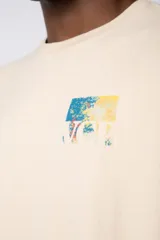 Remera de corte oversize color beige, confeccionada en algodón grueso. Presenta una estampa frontal pequeña con diseño artístico abstracto en tonos azules y amarillos.