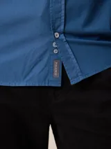 Camisa de manga larga en color azul, confeccionada en algodón con técnica de teñido garment dye. Presenta cuello abotonado, cierre frontal con botones y un bolsillo en el pecho con detalle bordado.