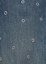 Jeans de tiro medio y corte barrel con diseño de ojales metálicos distribuidos por toda la prenda. Cuenta con cinco bolsillos, cierre de botón y cremallera, y trabillas para cinturón.
