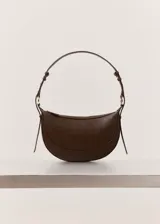 Bolso de hombro de tamaño mediano con diseño ovalado tipo media luna, en color marrón oscuro texturizado. Cuenta con asa ajustable, cierre de cremallera y herrajes metálicos dorados.