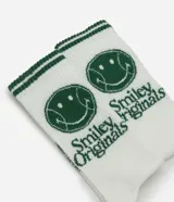 Medias de caña larga color blanco con detalles en verde, que incluyen un estampado de carita sonriente y el texto 'Smile Origins' en el lateral. Cuentan con franjas verdes en el borde superior.