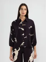 Camisa de manga 3/4 con puños elastizados, cuello camisero y estampado de figuras humanas y peces en color crema sobre fondo negro.