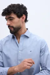 Camisa de manga larga fit semi slim, color celeste melange, con cuello camisero, cierre frontal de botones y pequeño bordado de ave en el pecho.