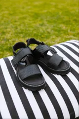 Sandalias de cuero negro con textura de serpiente, diseño de tiras anchas, cierre de velcro, suela flatform dentada y puntera cuadrada.